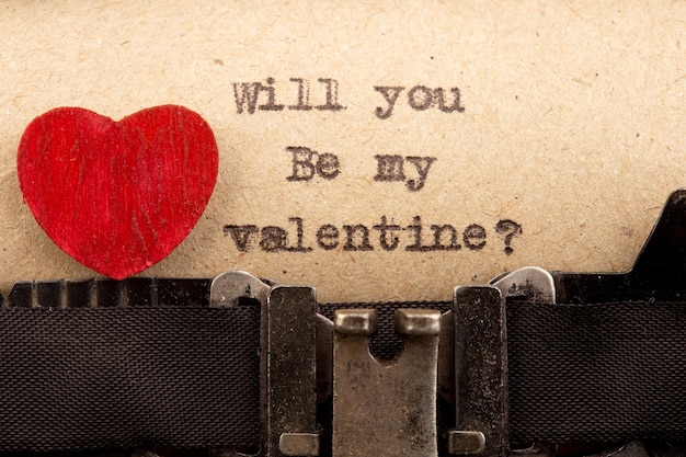 Will you be my Valentine phrase on typewriter Valentines Day greetings concept Little red wooden heart close up Valentines greeting card