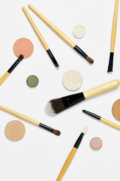 Willekeurig gerangschikte professionele make-upborstels, met naakt oogschaduwpalet, dat op witte achtergrond wordt geïsoleerd. Bovenaanzicht, flatlay. Het concept van make-up en cosmetica, gezicht.