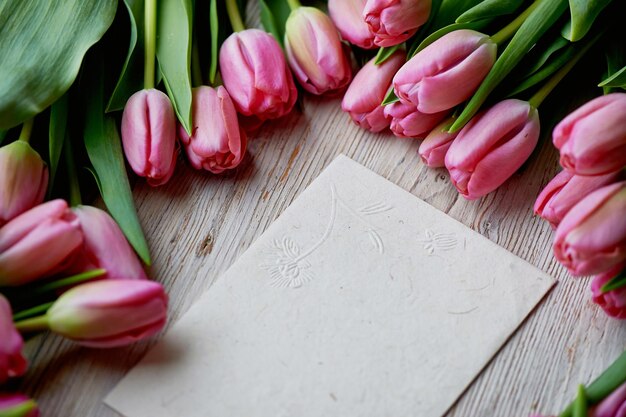 Willekeurig verspreide roze tulpen lagen op een Kraft-envelop met houten structuur