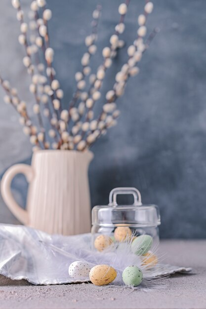 Willow branches in a vase on a gray background and colored chocolate eggs for the Easter holiday.