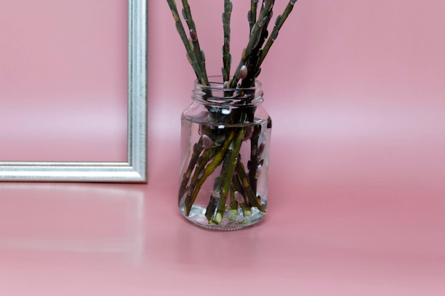 The willow stands in a jar of water near the frame on a pink background