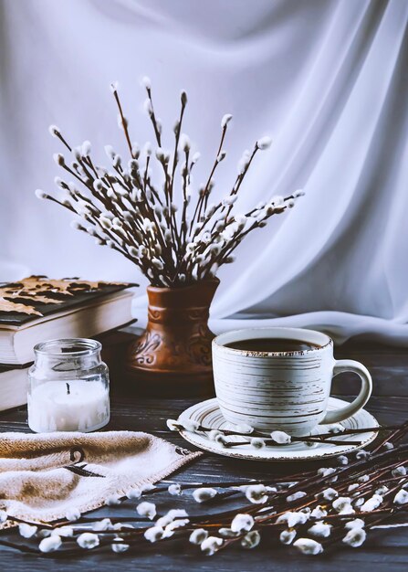 Willow twigs cup of coffee books and candle Spring still life on a white and wooden background