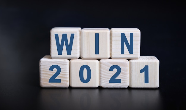 WIN 2021 text on wooden cubes on a black background with reflection.