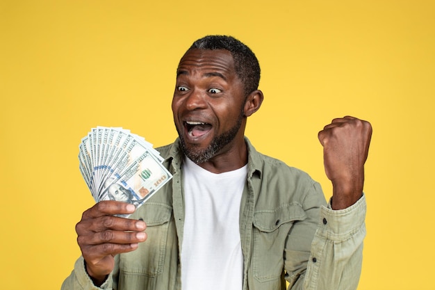 Win cashback finance and profit Glad excited adult black guy with open mouth hold many dollars