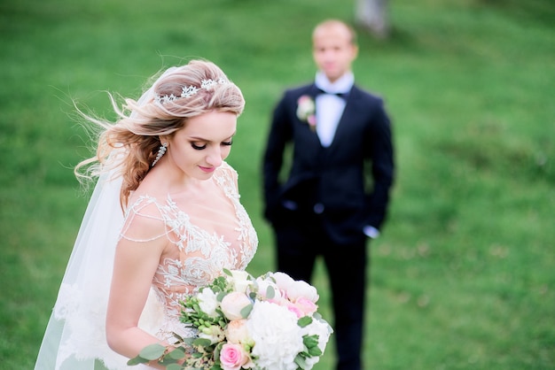 写真 彼女は新郎の前に緑の芝生に立っている間に風が花嫁の髪を吹き飛ばします