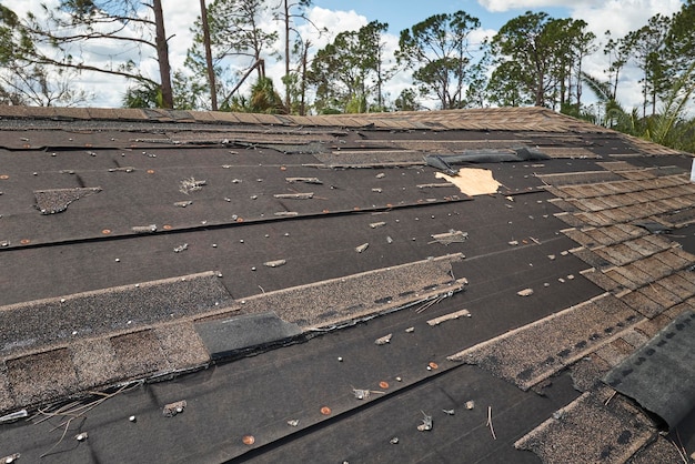 Wind damaged house roof with missing asphalt shingles after hurricane Ian in Florida Repair of home rooftop concept