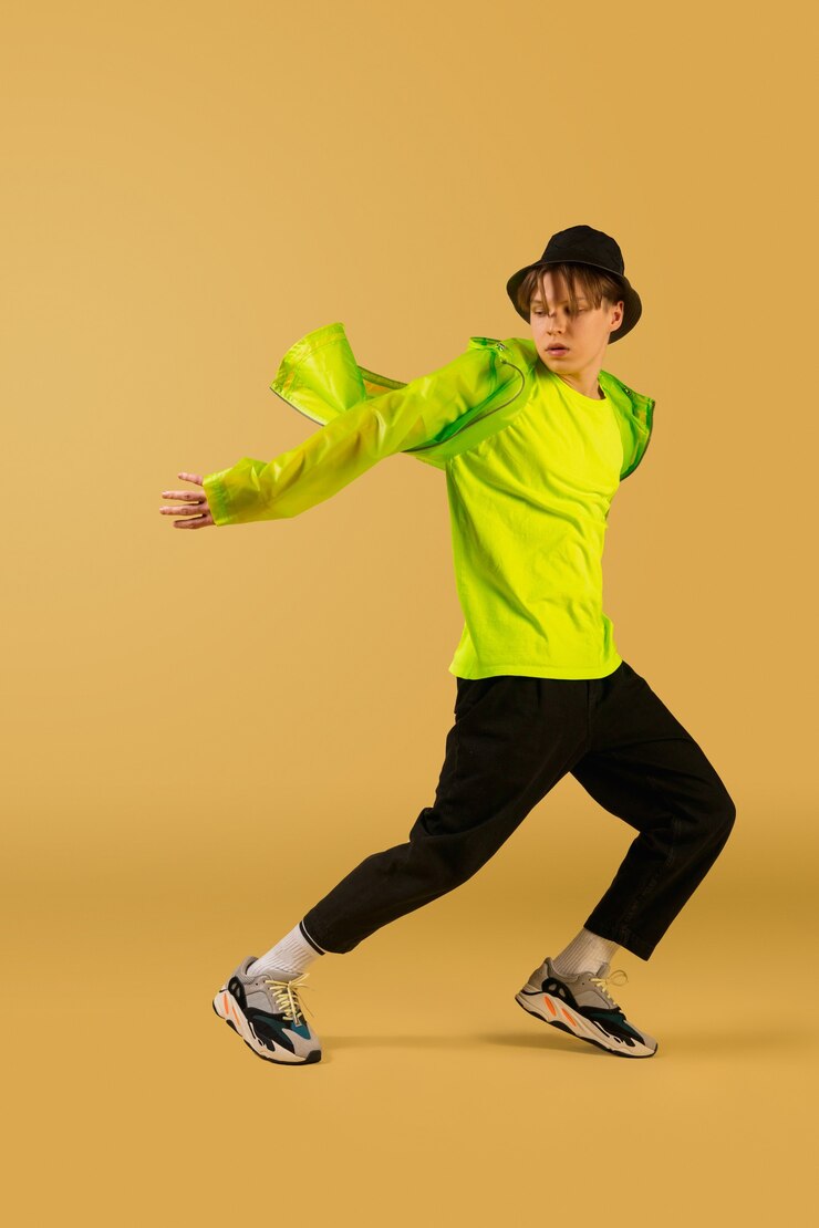 Photo 風。黄色のスタジオの背景に分離して踊る昔ながらの若者。アーティストのファッション、モーションとアクションのコンセプト、若者文化、ファッションの復活。若い白人の巻き毛の少年。