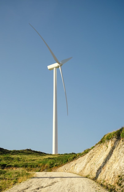 Wind turbine on hill generating electricity over a blue sky background. Clean and ecological energy production concept.