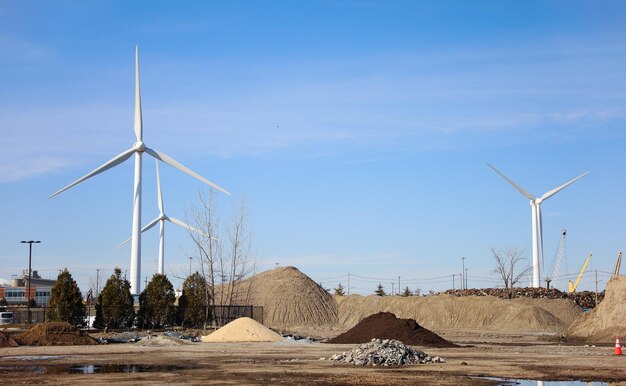 Wind turbines are seen in front of a pile of sand.