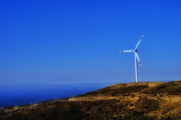 Wind turbines on land by sea against clear blue sky