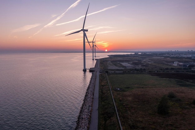 Wind turbines at sunset. Green ecological power energy generation. Wind farm eco field. Offshore and onshore windmill farm green energy at sea.