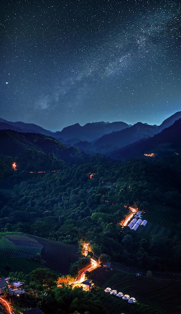 天の川の背景を持つ星空の夜の車から長時間露光トレイルライトトラックと曲がりくねった山道