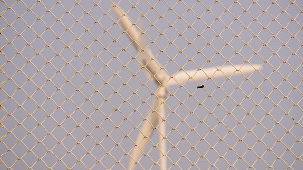 Фото Ветряная мельница, виденная через цепной забор на фоне ясного неба