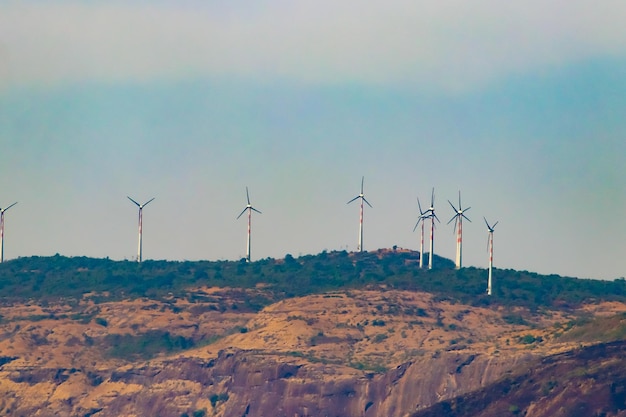 Photo windmills on the green tree mountain with blue sky