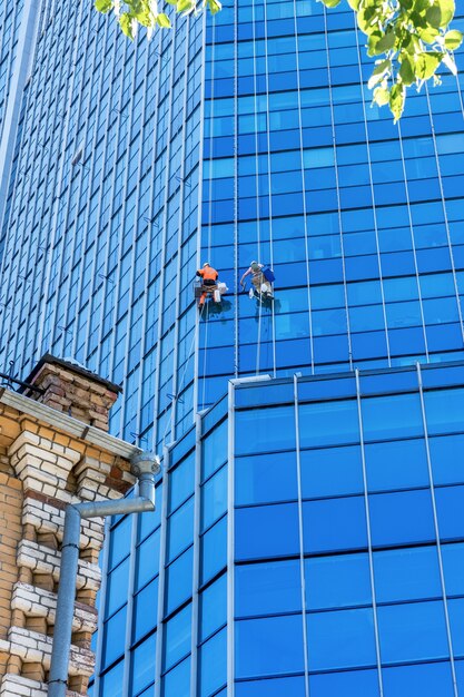 Window cleaners wash the glass on the wall of an office building in a skyscraper in the city center Dangerous and difficult work in a big city