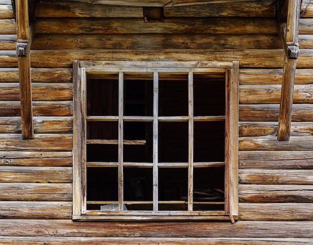 Window frame with broken glass in the wall of an old abandoned wooden house