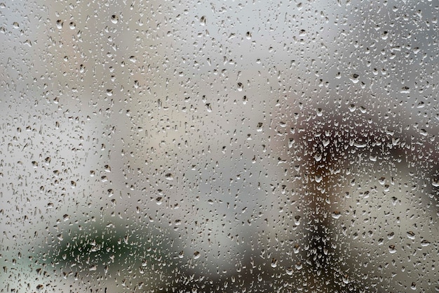 стекло окна с каплями дождя, показывающее размытый город на заднем плане