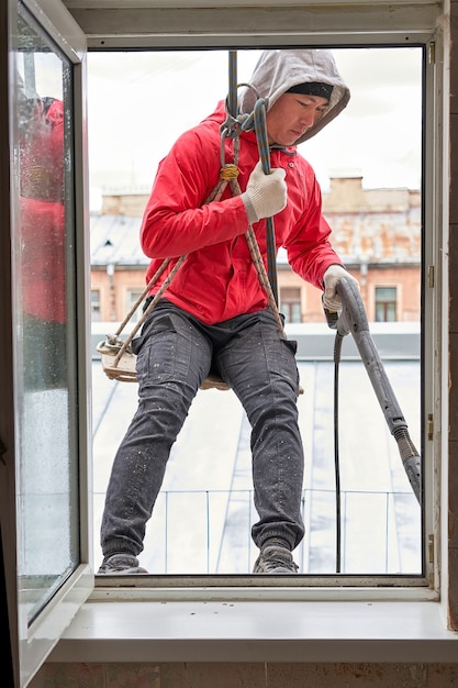 A window washer in climbing gear hangs in the window\
opening