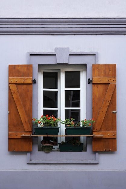 開いている木製の雨戸とその前に花が飾られた窓