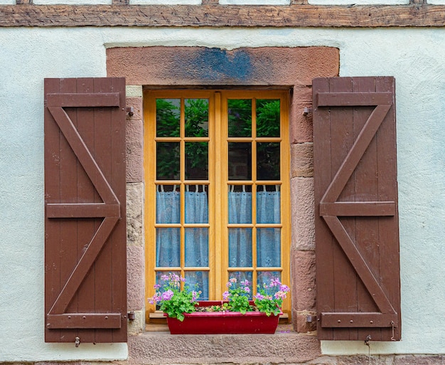 A window with a red flower box and a window with a window with a wooden shutter.