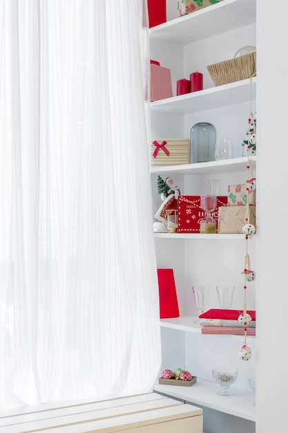 A window with white curtains and shelves on the sides that hold Christmas gifts