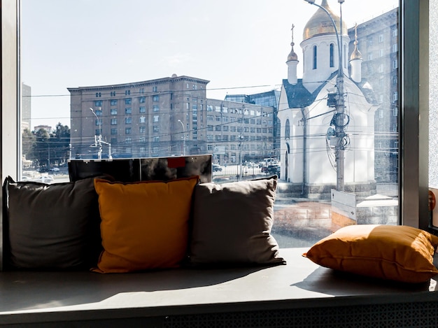 Photo a window with a windowsill on which pillows lie with a view of the city and the attraction of a small chapel with a golden dome in novosibirsk