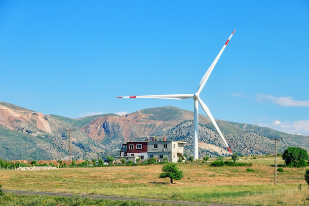 Windturbine en huis op heuvel onder blauwe hemel