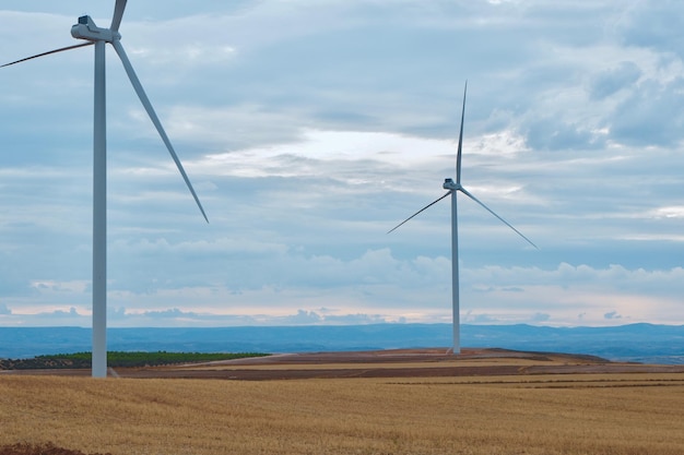 Windturbines op een gesneden veld met dramatische cloudscape Alternatieve energiegeneratoren tegen blauwe lucht met wolken in de regio Teruel Aragon Spanje Elektriciteitsproductiesite