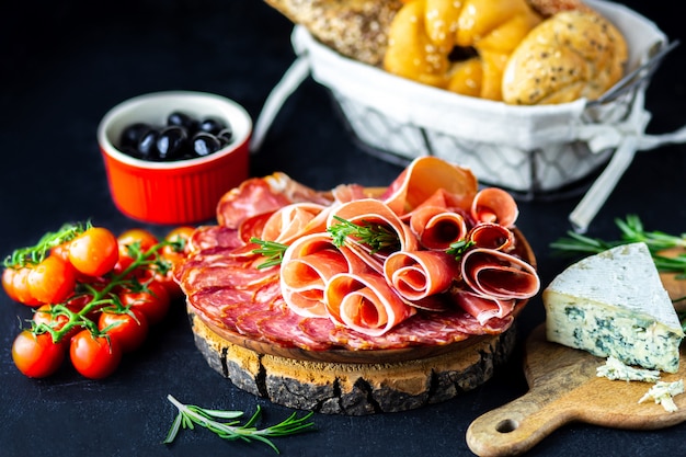 Wine appetizer on a wooden board. white wine cheese, jamon, prosciutto, with salami and olives on a black background. freshly baked bread with cheese and wine snacks. Tasty party snacks