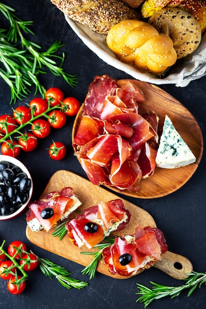 Wine appetizer on a wooden board. white wine cheese, jamon, prosciutto, with salami and olives on a black background. freshly baked bread with cheese and wine snacks. Tasty party snacks