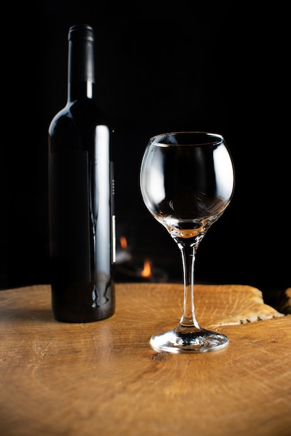 Wine bottle and empty glass on rustic wooden surface with fire behind