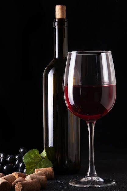 Wine bottle and glass of red wine on dark textured surface