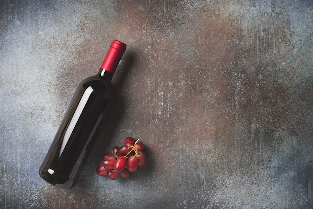 Wine bottle and grape on stone dark background, copy space, top view