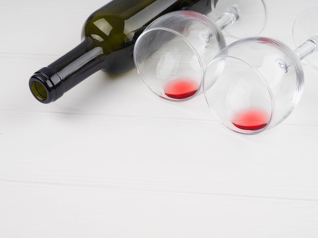 A wine bottle lies, next to two glasses with remnants of red wine