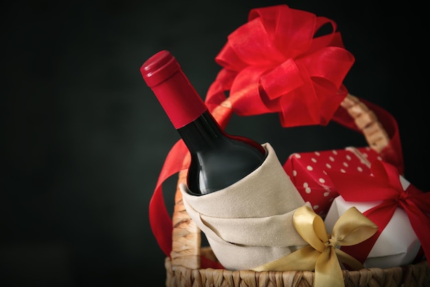 Photo wine bottle with gift boxes in wicker basket on dark background