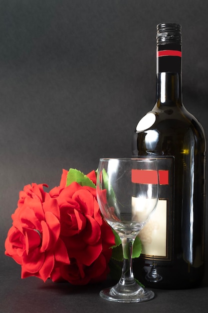 Wine bottle with a glass and a red rose on a black background