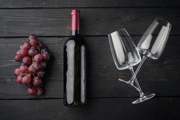 Bottiglia di vino con set di uva, sul tavolo in legno nero, vista dall'alto laici piatta