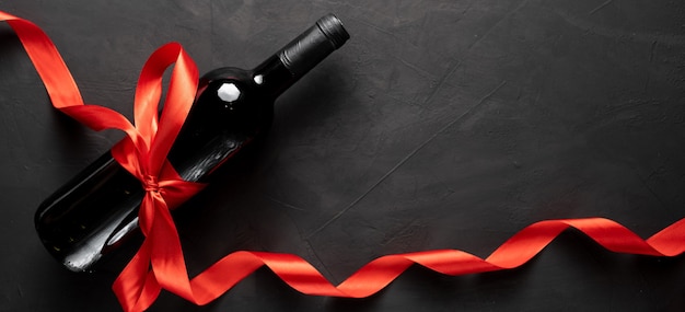 Wine bottle with a red satin ribbon bow. Valentine's Day. On a concrete background. Free space for your text.