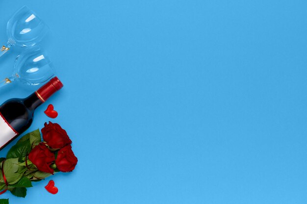 Wine bottle with roses and wine glasses on blue background top view. Valentine day