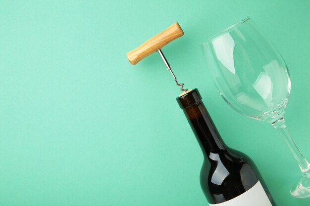 Wine bottle with wine glass and corkscrew lying on mint background space for text top view