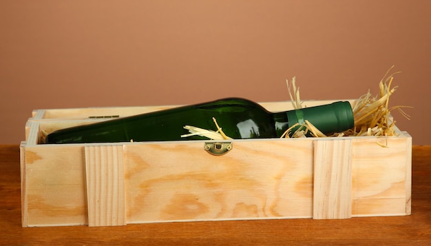 Wine bottle in wooden box on wooden table on brown background