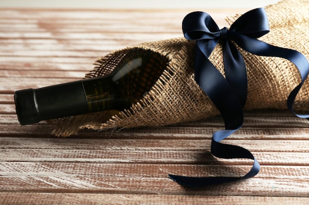 Wine bottle wrapped in burlap cloth on wooden planks background