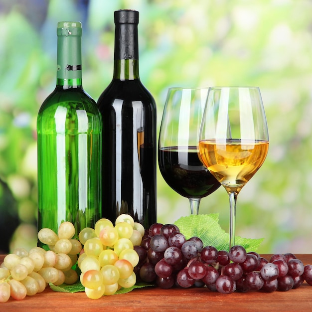 Wine bottles and glasses of wine on bright background