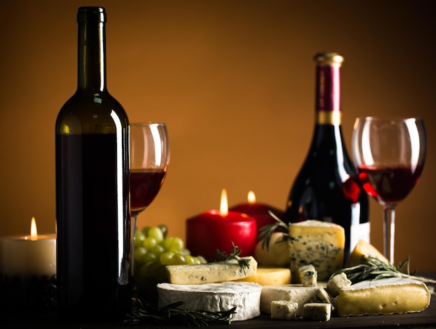 Бутылки вина, бокалы для вина, зажженные свечи, сыры и виноград на коричневом фоне