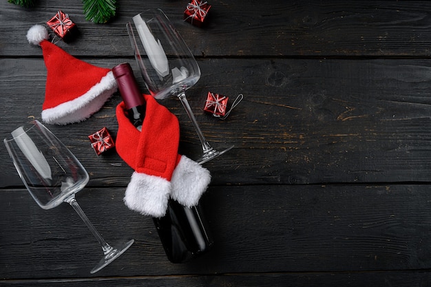 Bottiglie di vino con set di cappelli rossi di babbo natale, su sfondo di tavolo in legno nero, vista dall'alto piatta, con spazio di copia per il testo