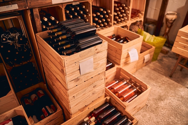 나무 상자에 알코올 음료의 유리 병과 빈티지 년 레이블이있는 와인 랙이있는 와인 저장고