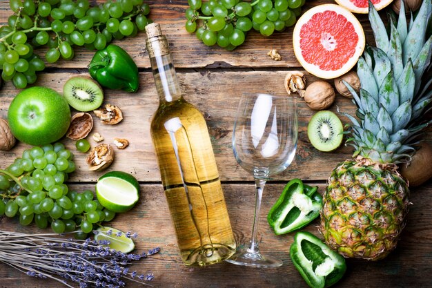ワインのコンセプト。緑のブドウ、グレープフルーツ、古い木製のテーブルの他の果物と若い白バイオワインのボトルとグラス