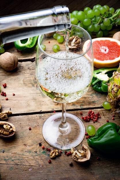 Wine concept. Glass of young white bio wine with green grapes, grapefruit and other fruit on an old wooden table