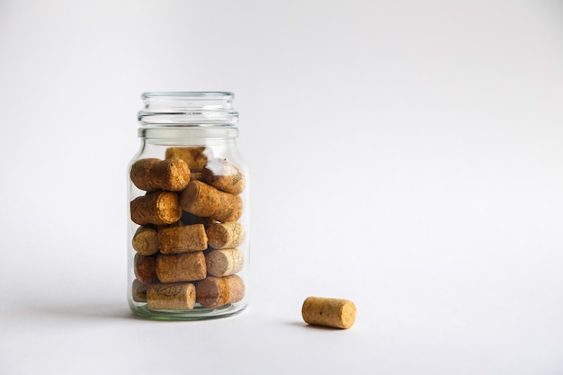 Wine corks lie in a glass jar on a white background