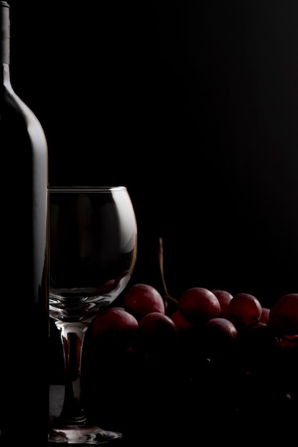 Photo wine glass,  bottle of wine with  and red grapes on a dark.